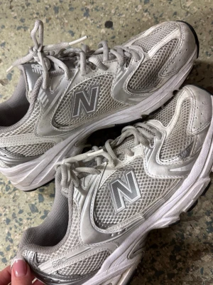 Grå New Balance 530 sneakers - Säljer ett par New Balance 530 sneakers i ljusgrått med silvriga detaljer. Skorna har meshpaneler för extra ventilation, snörning och en platt sula med svart yttersula. Ikoniska 'N'-loggan på sidorna och ABZORB-dämpning för skön komfort. Perfekt för dig som gillar retrostil och sportig vibe.