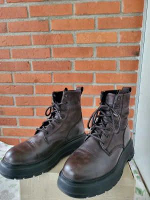 Bruna boots från Vagabond i skinn 41 - Chunky bruna boots från Vagabond i äkta skinn med kraftig svart platt sula och snörning framtill. Klassisk rund tå och högt skaft ger en cool och robust look. Perfekta för dig som gillar stilrena och tidlösa skor med edge. Passar mig som brukar ha storlek 42