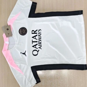 PSG fotbollströja och shorts Jordan - Snygg PSG fotbollströja i vitt med svarta och rosa detaljer, kortärmad och med Jordan-logga samt Qatar Airways-tryck. Matchande svarta shorts med rosa inslag och PSG-emblem. Tillverkad i lätt och ventilerande material, perfekt för träning eller match.
