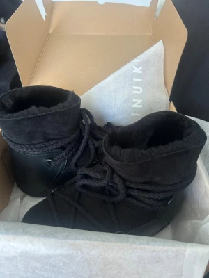 Svarta Inuikii boots med snörning - Säljer ett par svarta Inuikii boots med snörning och rund tå. Skorna har en kombination av mocka och skinn, samt ett varmt foder som gör dem perfekta för kalla dagar. Helt ny, aldrig använda. 