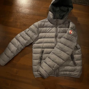 Grå Colmar pufferjacka med huva - Säljer en grå pufferjacka från Colmar med huva och dragkedja framtill. Jackan är varm och skön till vintern, storlek 48 som motsvarar ungefär strlk ”S” Schysst grå färg utvändigt och en skön lite grönaktig färg innuti. Litet märke insida ärm( se bild) inget som syns när du har på jackan. Bra skick annars, pris kan diskuteras. Person på bild ca180 cm lång