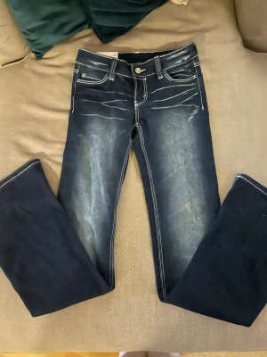 Cheap Monday Booty Bell jeans 25/32 - Snygga blå Booty Bell jeans från Cheap Monday med tydliga vita sömmar och broderade bakfickor med C och M. Jeansen har bootcut-modell, låg midja och klassisk tvättad denimlook. Perfekta för dig som gillar retrovibbar och markerade detaljer.