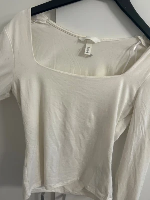 Vit långärmad topp från H&M - Säljer en stilren vit långärmad topp från H&M med fyrkantig urringning. Toppen är i mjuk bomull och har en clean, enkel look som är lätt att matcha. Perfekt för dig som gillar minimalistisk stil och vill ha en basic i garderoben.