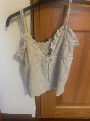 Vit broderad linnetopp från 157 - Säljer en söt vit linnetopp från 157 i storlek XS. Toppen har broderade hålmönster, volangdetaljer vid axelbanden och en knytning framtill. Perfekt för varma dagar och ger en romantisk vibe med sin lätta bomullskänsla.