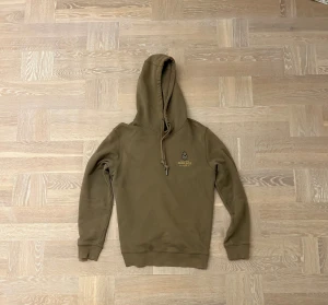 Beige hoodie från Morris med tryck - Snygg beige hoodie från Morris med broderat emblem och text på bröstet. Tröjan har huva med snörning och långa ärmar. Tillverkad i mjuk bomull som är skön att ha på sig. Perfekt för dig som gillar stilrena och klassiska plagg.