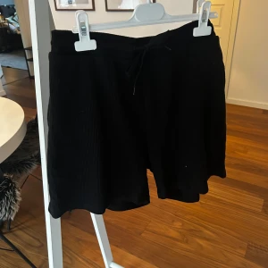 Svarta ribbade shorts med snörning - Svarta shorts i ribbat material med avslappnad passform och snörning i midjan. Perfekta för chill dagar eller när du vill ha något bekvämt. Tjockare tyg som ger en skön känsla och snygg struktur.