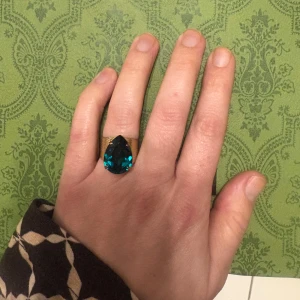 Caroline Svedbom ring - Statementring från Caroline Svedbom med bred, guldfärgad band och en stor, droppformad sten. Ringen har en snygg textur på metallen och är perfekt för dig som vill sticka ut med accessoarerna.