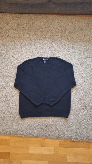 Marinblå stickad tröja från Chaps - Snygg varm marinblå stickad tröja från CHAPS i storlek XL, men skulle nog säga den passar mer som L. 100% bomull. Använd fåtal gånger och skicket är i princip som ny, inga defekter eller slitningar finns. Den har rund krage och passar perfekt nu under vintern och Jul! Skick: 9/10