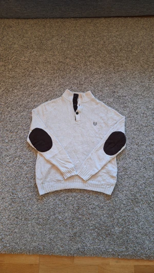 Beige kofta från Chaps med knappar - Riktig snygg beige stickad tröja med halvpolokrage från CHAPS i storlek S. 100% bomull. Använd fåtal gånger och skicket är som ny, inga defekter eller slitningar finns. Den har tre knappar passar perfekt när du vill vara lite mer elegant. Skick: 9/10