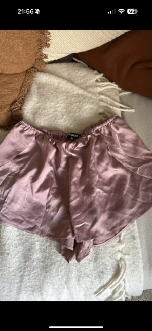 Ljusrosa silkesliknande shorts Moss Copenhagen - Säljer ett par ljusrosa shorts från Moss Copenhagen med glansig finish och bred resår i midjan. De har en loose passform och är tillverkade i ett silkesliknande material som känns mjukt mot huden. Perfekta för varma dagar eller chill hemma.
