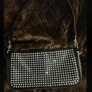 Svart axelväska med glittriga stenar - Snygg svart axelväska med massor av glittrande stenar på framsidan. Mått 19x12x3