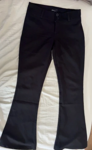 Svarta bootcut-byxor från Gina Tricot - Snygga svarta bootcut-byxor från Gina Tricot i storlek M. Byxorna har två knappar fram, bälteshällor och fickor med knapp bak. Materialet är mjukt och har en lätt stretch. 
