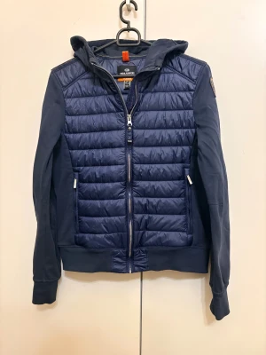 Mörkblå pufferjacka från Parajumpers - Säljer den pga för liten på mig, jag behöver pengarna akut, 100% äkta we koden visar äkthetskapen. Snygg mörkblå pufferjacka från Parajumpers med quiltad front och mjuka ärmar. Jackan har huva, dragkedja och coolt patch på ärmen. Materialmix med fleece och syntet, perfekt för kyliga dagar. Stilren design med praktiska fickor och detaljer. 