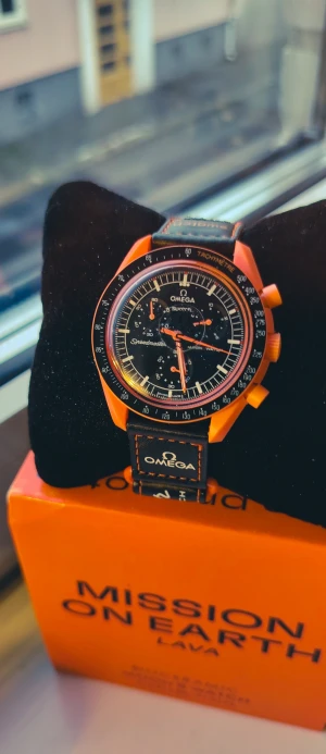 Omega x Swatch Speedmaster Lava helt ny i box - Omega x Swatch Speedmaster Mission on Earth Lava med orange boett och svarta detaljer. Klockan har en rund form, svart urtavla med vita och orange visare samt tachymeter-skala. Snyggt svart textilband med orange sömmar och Omega-logga. Biokeramisk konstruktion. Helt ny med tag, plastfilm och papper förseglade med låda. . 