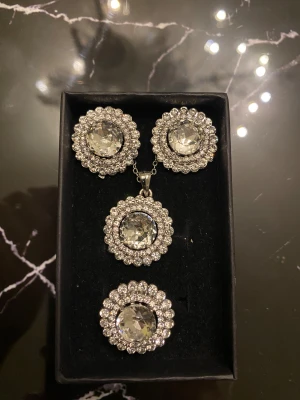 Smyckesset i presentask - Fint set med halsband, örhängen och ring. Ringen är justerbar i storlek. Strass och stor diamant i mitten. 