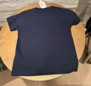 Blå Comme des Garçons Play t-shirt - Snygg mörkblå t-shirt från Comme des Garçons Play med stort vitt hjärta och rött hjärtdetalj med ögon på bröstet. Klassisk rund hals och korta ärmar. Tillverkad i 100% bomull, mjuk och skön kvalitet. Perfekt för dig som gillar statement-plagg.