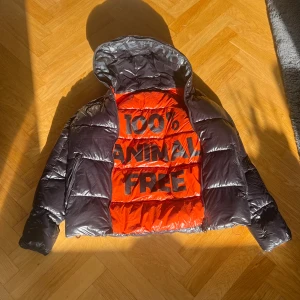 Svart pufferjacka Save The Duck - Jätte Snygg svart pufferjacka från Save The Duck med glansig finish och huva. Jackan har dragkedja framtill och två fickor med dragkedja. Perfekt för kalla dagar och har en modern vibe.  Ny pris ca 3000kr. Med luva 97cm lång, utan luva 72cm lång  och armarna. 66cm.                                 !!!!!!   : Den har bara en liten skada på armen men inte jätte mycket som syns. Fråga om bild gärna.