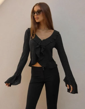 Svart omlott blus med volang - Säljer en svart blus med omlott-design och volangdetaljer längs v-ringningen och ärmsluten. Blusen är croppad och har långa, utsvängda ärmar som ger en cool och trendig look. Materialet är lätt och har en skrynklig struktur.