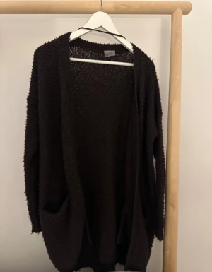 Mörklila kofta från Vero Moda - Mysig mörklila kofta från Vero Moda i storlek S. Koftan har en loose passform, långa ärmar och två praktiska fickor framtill. Materialet är stickat och har en fluffig, lite grov struktur.