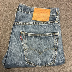 Levi's 501 Premium blå jeans straight - Levi's 501 Premium jeans i klassisk blå tvätt med raka ben och normal passform. Ikonisk läderpatch bak, fem fickor och gul kontrastsöm. Tillverkade i slitstarkt jeanstyg med knappgylf. Perfekt för dig som gillar tidlös stil och vill ha ett par jeans som alltid funkar.