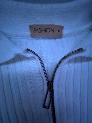 Vit ribbad tröja med dragkedja - Vit långärmad tröja från Fashion med ribbad struktur och klassisk krage. Tröjan har en half zip-dragkedja framtill som ger en chill och sportig vibe. Materialet känns mjukt och är troligen stickat, perfekt för lager på lager. Enkel och clean design som funkar till många stilar. Skriv om du har frågor 