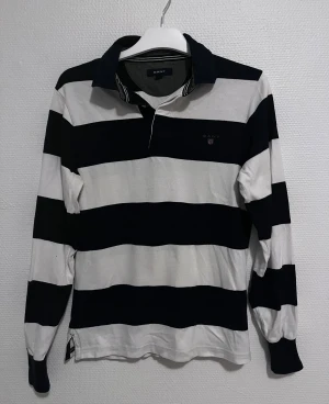 Randig pikétröja från GANT XS - Snygg långärmad pikétröja från GANT i storlek XS. Tröjan har breda marinblå och vita ränder. Perfekt för dig som gillar att ha något som sticker ut.