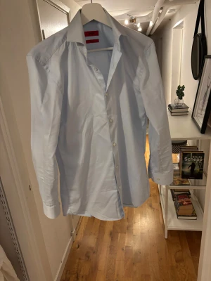 Ljusblå slim fit skjorta Hugo Boss - Snygg ljusblå skjorta från Hugo Boss med slim fit-passform och klassisk krage. Skjortan har långa ärmar, vita knappar och är tillverkad i bomull som är lätt att stryka. Perfekt för dig som gillar stilrena och cleana plagg.