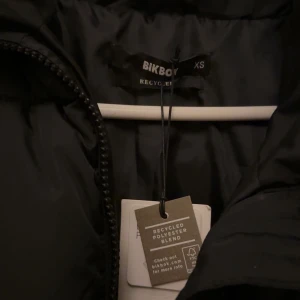 Svart pufferjacka från Bikbok XS - Svart pufferjacka från Bikbok i storlek XS. Jackan har en hög krage, breda quiltade sektioner och dragkedja framtill. Tillverkad av återvunnen polyesterblandning, perfekt för kalla dagar. Enkel och stilren design som funkar till många olika looks.