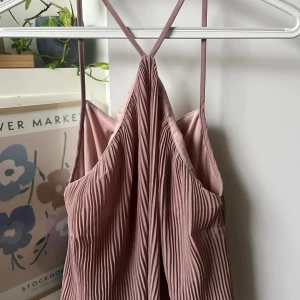 Plisserad ljusrosa linnetopp - Säljer en plisserad ljusrosa linnetopp med tunna axelband som korsas i ryggen. Toppen har en flowy och luftig passform, perfekt för varma dagar. Materialet känns mjukt och har en snygg struktur med vertikala veck. Supersnygg att styla med jeans eller kjol! Helt oanvänd! 