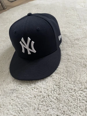 New Era keps  - Snygg marinblå New Era 59FIFTY keps med klassiskt New York Yankees broderat vitt logotyp framtill. Platt skärm och MLB-logga baktill. Tillverkad i polyester, perfekt för dig som vill ha en clean och sportig look.