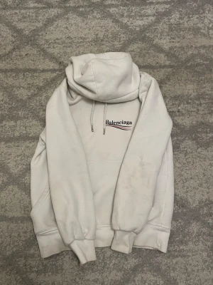 Vit hoodie  - Vit hoodie från med svart och rött tryck på bröstet och ryggen. Tröjan har huva med snörning, ribbade muddar och en klassisk loose passform. Perfekt för dig som gillar streetwear och vill ha en clean look med designer vibe.