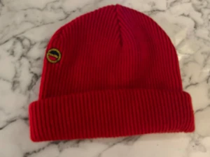 Röd ribbad mössa med broderad patch vintage  - Snygg röd mössa med ribbad stickning och uppvikt kant. På sidan sitter en broderad patch i gult och svart som ger extra attityd. Perfekt för dig som vill sticka ut med färg i vinter. Materialet är mjukt och stickat, passar dig som gillar streetwear. Har tyvärr klippt bort etiketten men det är en Busnel vintage 