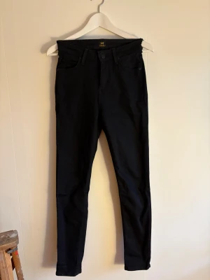 Svarta Lee Scarlett High jeans W27 L31 - Säljer ett par svarta Lee Scarlett High jeans med hög midja och skinny fit. Klassisk femficksmodell med Lee-logga på bakfickan och knapp. Jeansen är tillverkade i bomull med lite stretch för extra komfort.