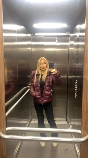 Vinröd pufferjacka med dragkedja - Säljer en vinröd pufferjacka med hög krage och dragkedja framtill. Jackan har en quiltad design och två sidofickor. Perfekt för kalla dagar och har en snygg, lite glansig finish. Passformen är normal och jackan är långärmad.