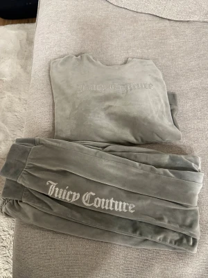 Gråa mjukisdress från Juicy Couture barn 12/13 år - Supermjuka gråa mjukisbyxor från Juicy Couture i velour med bred resår i midjan och glittrig broderad logga längs benet. Har används men inga övertydliga tecken på slitage, har tagit bilder på det som finns!  Storlek är 12/13 år! Men skulle säga att det passar en 10 åring oxå beroende på längd.