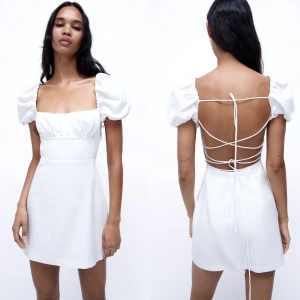 Vit kortklänning från Zara  - Supersöt populär vit kortklänning från Zara med puffiga kortärmar och fyrkantig urringning. Klänningen har öppen rygg med snygg snörning som knyts baktill. Stilren och trendig passform, perfekt för studenten. Materialet känns lätt och luftigt.