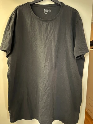 Svart t-shirt Basic You XXL - Svart t-shirt från Basic You i storlek XXL, tillverkad av 95% ekologisk bomull och 5% elastan. Modellen är klassisk med rund hals och korta ärmar, perfekt för en chill och enkel stil. Materialet är mjukt och skönt mot huden.