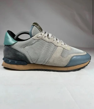 Valentino Rockrunner - Snygga Valentino Garavani Rockrunner sneakers i ljusgrå mesh och mocka med blå detaljer i skinn och en cool grön häl. Skon har snörning, platt sula och ikoniska nitar på hälen. Väldigt bra skick 