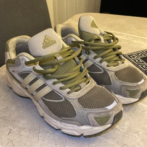 Grå och gröna sneakers från Adidas - Säljer ett par grå och gröna Adidas sneakers med snörning. Skorna har en robust sula och klassiska tre ränder på sidan. Perfekta för vardagsbruk och träning.