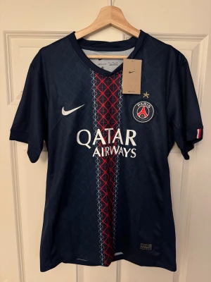 PSG matchtröja Nike D.Doué #14 - Säljer PSG-matchtröja från Nike med D. Doué #14. Marinblå med geometriskt mönster och röd/vit detalj i mitten. Kortärmad, lätt polyester och perfekt för fotboll. Qatar Airways-logga på bröstet och PSG-emblem med guldstjärna. Följ oss på Instagram: @kickstoreuf.