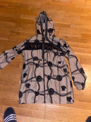 Beige Versace vindjacka  - Säljer min Versace vindjacka i storlek L normal passform men passar också M och S om man vill ha den lite längre som en lång vindjacka. Se sista bild!