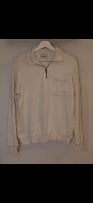 Vit half zip tröja från Woodbird XS - Vit långärmad tröja från Woodbird i storlek XS. Tröjan har en klassisk krage, half zip-dragkedja framtill och en bröstficka med diskret broderad logga. Materialet är mjukt och känns som bomull, perfekt för chill dagar.