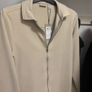 Beige ziptröja från Only & Sons - Snygg beige ziptröja från Only & Sons med prislapp kvar köpt för 599kr nypris. Clean och modern look på jackan.. Perfekt att slänga på sig när du vill vara chill men ändå se fräsch ut.