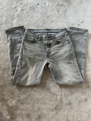 Levi's 501 ljusgrå jeans straight fit - Ljusgrå Levi's 501 jeans med klassisk femficksdesign och raka ben. Jeansen har normal passform och är tillverkade i bomull. Snygg tvättad look och ikonisk läderpatch bak i midjan. Perfekta för en avslappnad och stilren vibe. W25 L30. Modellen på bilden är 177  60 kg för referens . Hör gärna av dig vid frågor eller funderingar 😁
