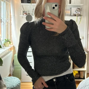 Glittrig polotopp  - Säljer en snygg polotopp från H&M i mörkgrått med glittrigt material. Toppen har puffade axlar, lång ärm och croppad passform. 