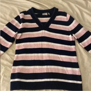 Randig stickad tröja - Säljer en stickad tröja med breda marinblå, rosa och vita ränder. 😇Tröjan har v-ringad hals med flätad kant, långa ärmar och ribbade muddar. Perfekt för dig som gillar söta tröjor☺️