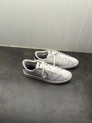 Vita sneakers från Adidas - Fräscha vita sneakers från Adidas med en klassisk design och blå detaljer på hälen. Tydlig Adidas-logga på både plös och häl. Skorna är endast använda ett fåtal gånger och är i mycket fint skick. Vid noggrannare titt kan man se mindre spår av användning, men inget som påverkar helhetsintrycket. (Pris kan diskuteras vid intresse.) 