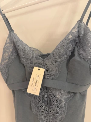 Grå spetsbody från Intimissimi - Supersnygg blå body från Intimissimi med tunna axelband och v-ringad spets upptill. Bodyn har dekorativ spets både fram och bak, vilket ger en extra lyxig känsla. Materialet är mjukt och stretchigt, perfekt för att känna sig bekväm och chic.