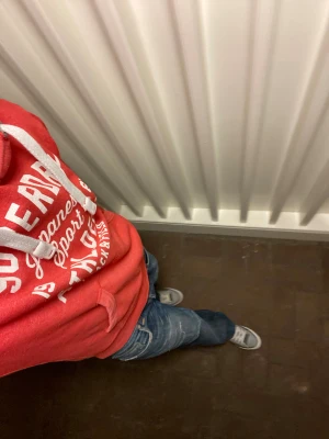 Superdry Hoodie - Röd hoodie från Superdry med vit text på bröstet och sportig känsla. Tröjan har huva med snörning, känguruficka och ribbade muddar. Inga defekter och den är som ny trotts att den är vintage. Om du undrar något är det bara att fråga✅🙌