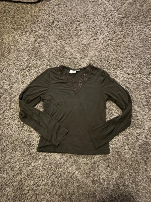 Mörkgrön långärmad topp med spets - Supersnygg mörkgrön långärmad topp från Gina Tricot med v-ringad hals och dekorativ spetskant i matchande färg. Toppen är i mjukt material och har en slim passform som sitter snyggt. Perfekt för dig som gillar detaljer och vill ha en stilren look.